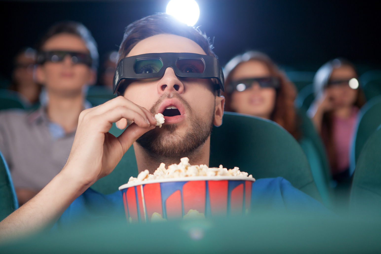 Ein Mann sitzt mit 3D-Brille im Kino und isst Popcorn, im Hintergrund weitere Besucher; Kurtz Detektei Stuttgart